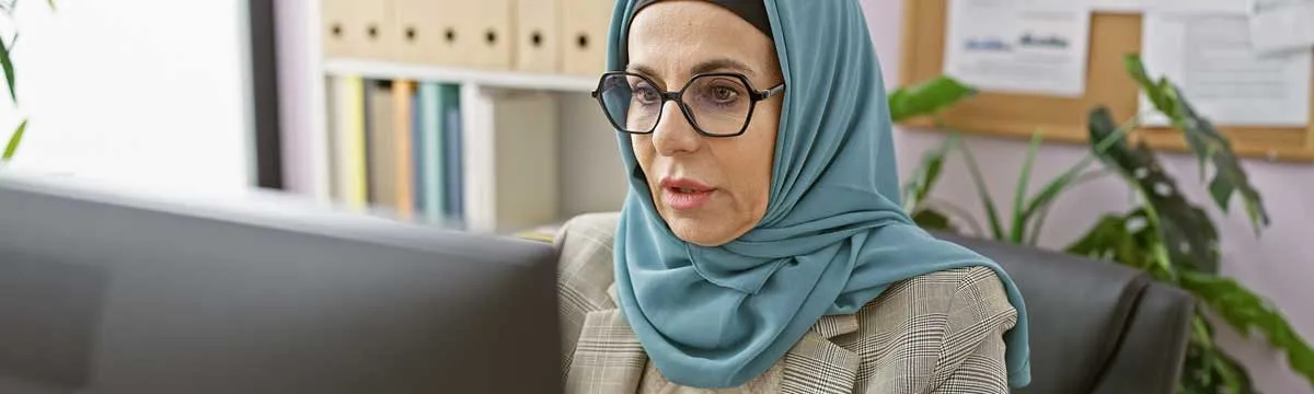 Eine Frau mit Kopftuch arbeitet in einer Büroumgebung am PC